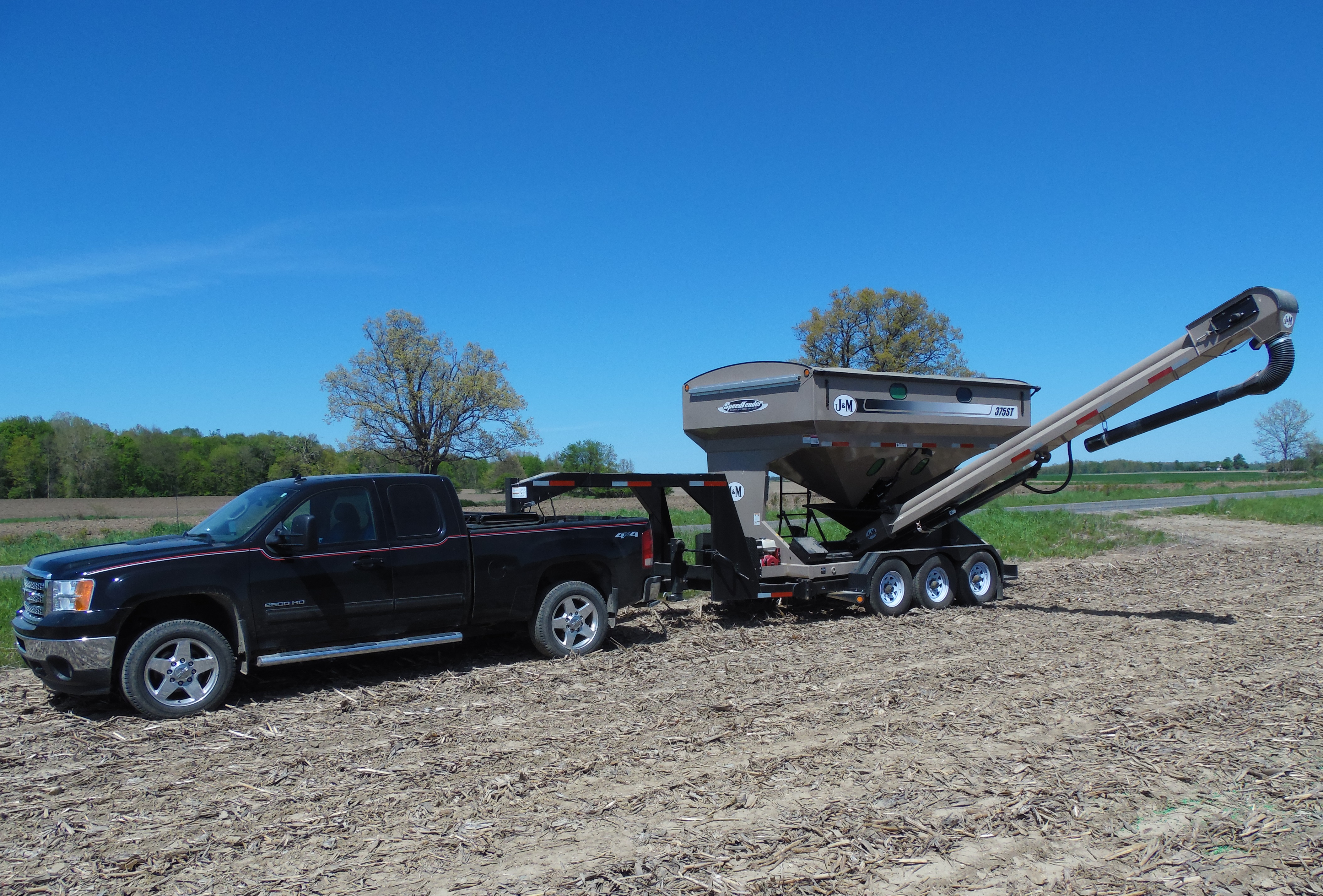 A black pickup truck towing a seed tender trailer in a harvested field.